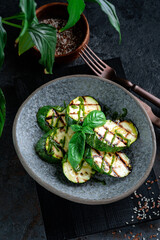 Grilled zucchini with pesto sauce. Vegetable dish with chopped zucchini on a gray plate served with basil