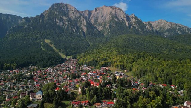 Astonishing aerial view with the rocky mountains filmed in cinematic style. Romanian landscape above Busteni city in a sunny day with blue sky