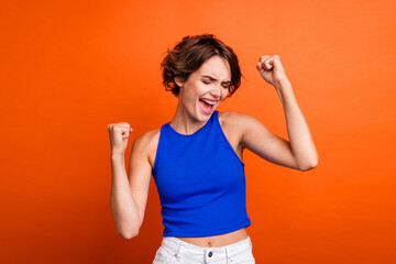 Photo of impressed lucky lady wear blue singlet screaming yeah rising fists isolated orange color background