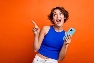 Photo of dreamy excited lady wear blue singlet texting shopping modern device pointing empty space isolated orange color background