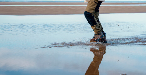 An energetic man in waterproof hiking boots walking along sea shore through water and puddles...
