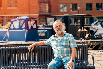 Portrait of f a mature man sitting on a bench at a quay enjoing last warm days of the autumn