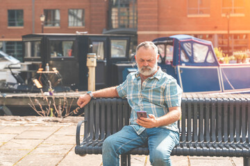 Mature man sitting on a bench and using a smartphone toned image