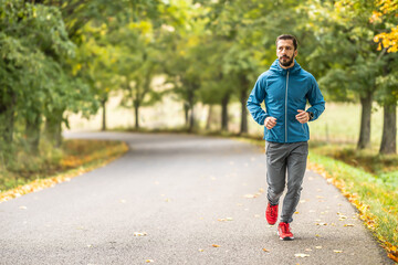 A young man is training and running in an autumn park.