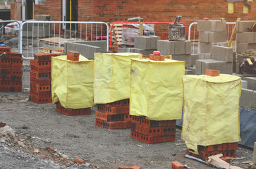 Red bricks and concrete blocks delivered on construction site and placed next to place of work ready for bricklayers - obrazy, fototapety, plakaty