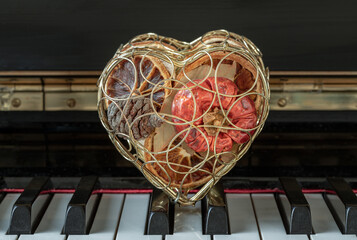 Fototapeta na wymiar Golden heart shaped mesh case is filled with dried fruits stand on the Piano Keyboard. Dried fruits in heart shaped metal case on keyboard, Christmas decoration, Melody of Love concept, Space for text