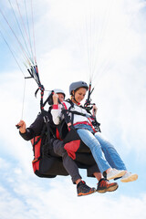 People, paragliding and happy in sky, together or extreme sport with freedom for fitness. Coach, partnership and person on adventure, helmet or fearless with backpack, parachute or flight with clouds
