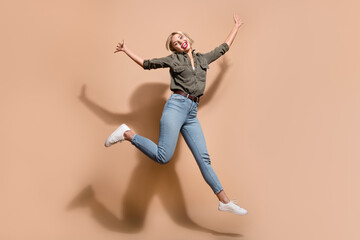 Fototapeta na wymiar Full length photo of carefree pretty lady wear khaki shirt jumping high having fun isolated beige color background