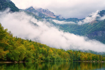 Bohinj lake (Bohinjsko jezero), Triglav national park, amazing autumn landscape, Slovenia. Scenic view of the clear water, Alps mountains with clouds and colored forest, outdoor travel background
