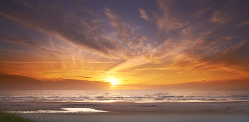 Seascape and landscape of a golden sunset on the west coast of Jutland in Loekken, Denmark. Beautiful cloudscape on an empty beach at dusk. Clouds over the ocean and sea in the evening with copyspace