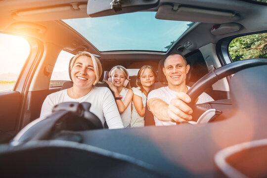 Happy young couple with two daughters inside car during auto trop. They are smiling, laughing during road trip. Family values, traveling concepts.