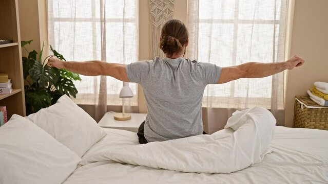 Young hispanic man waking up stretching arms at bedroom
