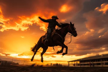 Fotobehang silhouette of a cowboy riding a horse in motion during a rodeo event against a sunset background © gankevstock
