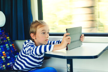 Cute child playing video games online on tablet during trip. Kid travels on a train.
