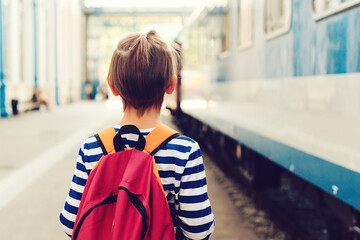 Boy waiting for express train on railway station platform. Kid with backpack on a subway.