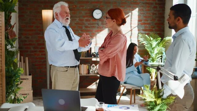 A senior director in his 70s advises and talks to a woman in the office during a break