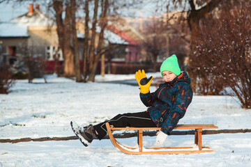 Boy with broken hand outdoors in winter park. Cute kid with broken arm and gypsum sitting on sled.