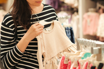 Pregnant woman chooses clothes for her future daughter. Mother doing shopping in baby shop.