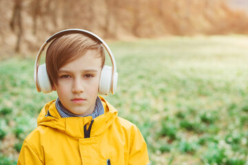 Sad boy listening to music at nature. Kid with headphones relaxing in the spring park. Upset boy with headphones on the walk.