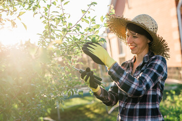 Side view of joyful young caucasian woman gardener cuts unnecessary branches and leaves from a tree...