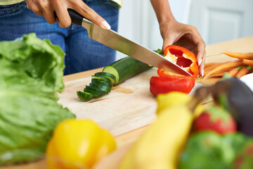 Woman, hands and cutting vegetables in kitchen on wooden board for healthy diet or vegetarian meal at home. Closeup of female person slicing natural organic red pepper for salad preparation at house