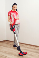 Young pregnant woman enjoys cleaning her house. Easy cleaning with a wireless vacuum cleaner.