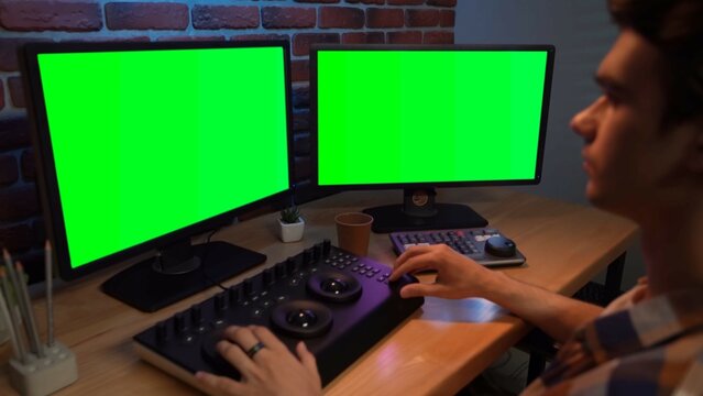 Closeup portrait of man working at the desk looking in chroma key monitors editing video settings using mixer.