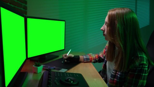 Portrait of young girl at the computer looking in chroma key monitors editing video using special equipment mixer.