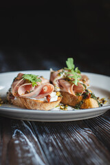 Appetizing bruschetta with thin pieces of meat on a dark background. Food photography.