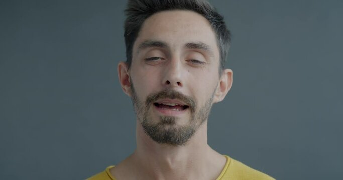 Close-up slow motion portrait of young man nodding head saying Yes expressing agreement on grey color background. People and communication concept.
