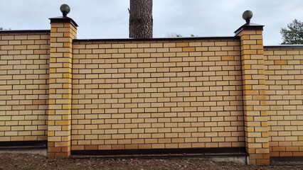 High stone modern fence made of yellow or white brick and columns with turrets. Background, texture, location © keleny
