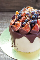 Delicious cake with figs dipped into melted chocolate, pecan nuts, grapes, chocolate bites and cookies on the top. Concept of autumn or summer cake