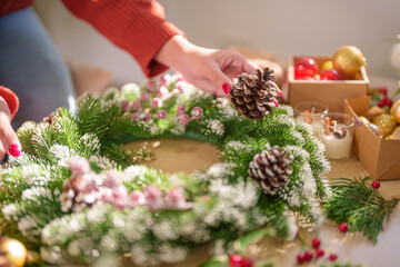 Woman making mistletoe wreath Christmas wreath decoration with hand made DIY winter greenery...
