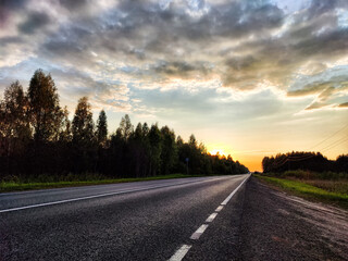 Dramatic sunset over asphalt road. The track goes into the distance in the evening summer, autumn or spring evening or night