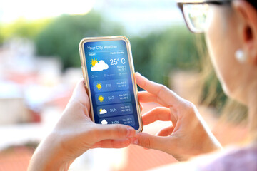 Woman outdoors checking weather forecast on her smartphone. - obrazy, fototapety, plakaty