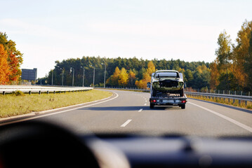 A cockpit view at the tow truck in motion with a damaged classic vehicle after being in a traffic accident. Emergency roadside assistance. Retro car renovation project. Vintage car recovery.
