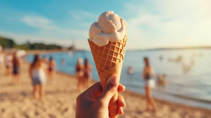 Foto auf Alu-Dibond A person holds a vanilla gelato cone on a sunny beach with friends and family in the background, capturing a perfect summer day. © B & G Media