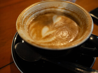 Half of the cappuccino has been drunk in a black glass with a black saucer.