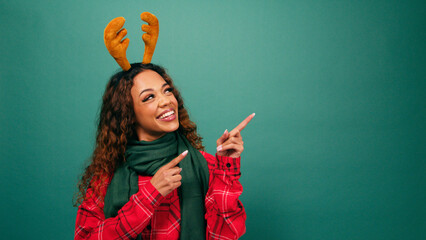 Beautiful young woman pointing left to copy space, reindeer ears studio