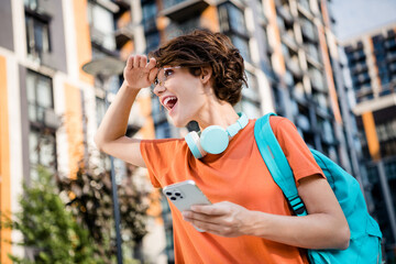 Photo of sweet excited girl dressed orange t-shirt eyewear backpack looking route modern gadget app outdoors urban town park