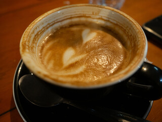 Half of the cappuccino has been drunk in a black glass with a black saucer.