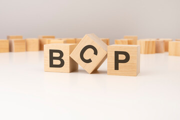 three wooden cubes with BCP symbols on them. white background. in the background there are many wooden blocks of different sizes