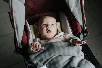 Obraz na płótnie Canvas Funny newborn Caucasian baby boy lying in a stroller indoors