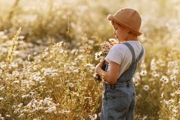 Portrait of a girl in a hat and denim overalls with a bouquet of daisies in a field. Concept of...