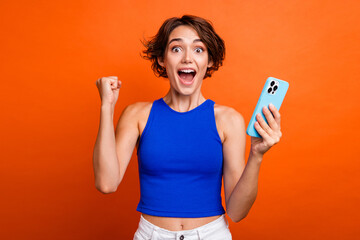 Photo of lucky impressed lady wear blue singlet rising fist online discount shopping modern device isolated orange color background