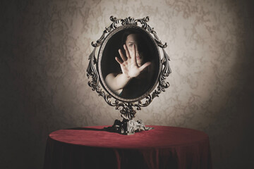 mirror reflecting a woman opening her hand in a stop sign; abstract concept