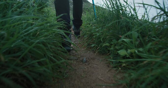Gimbal stabilized shot of person feet in hiking waterproof boots on laces walk on secluded mountain trail. Hiking in epic scenery, green rocky path. Inspiring adventure lifestyle,backpacking in nature