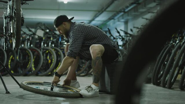 Mechanic sitting in garage, pumping tire on wheel and checking it while repairing bicycle