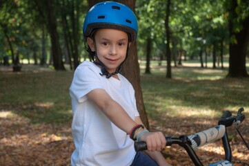 Obraz premium Caucasian boy with a sports helmet sitting on a bike in the park. About six years old.