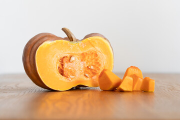 Half of an orange pumpkin next to diced pumpkin pulp on a wooden kitchen table.